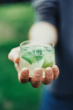 Hand holding Caipirinha cocktail outdoors