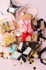 Holiday set of gift present boxes wrapped in craft paper and tied with bows on pink background, decorated with confetti. Birthday, Christmas, New Year, Mother day and sale concept, copy space