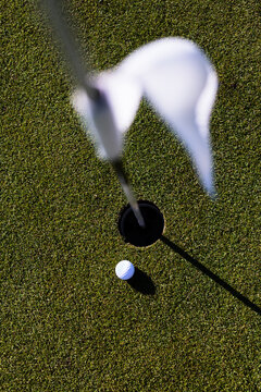 Golf ball on course putting green near hole with flag