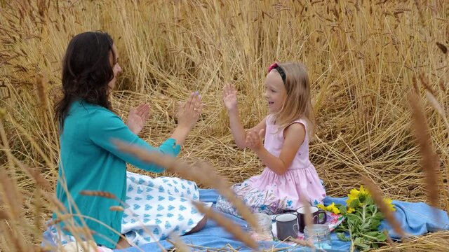 Little Girl with Mom Having Fun while Picnicking in a Wheat Field in a Summer Day. Slow Motion. Happy Childhood, Mothers Day Holiday and Enjoying Nature Concept