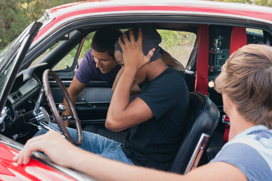 Three young men examine the interior of a classic car