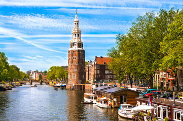Montelbaanstoren Sunny summer morning on Amsterdam Canal with boats and bicycles and houseboats. The Montelbaanstoren is a tower on bank of the Oudeschans – a canal in Amsterdam. - obrazy, fototapety, plakaty
