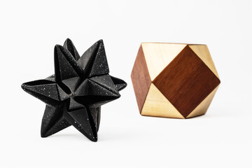 Small paper stellated dodecahedron next to wooden cuboctahedron on white background.