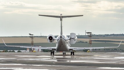 White small private twin-engine business jet on airport apron. Back side view. Dramatic clouds,...