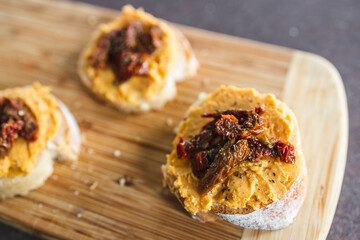 plant-based food, vegan snack with paprika hummus on sliced baguette bread topped with sundried tomatoes