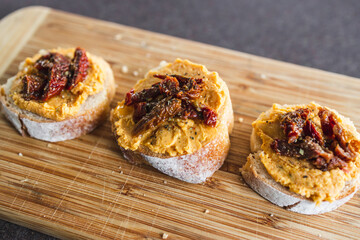 plant-based food, vegan snack with paprika hummus on sliced baguette bread topped with sundried tomatoes