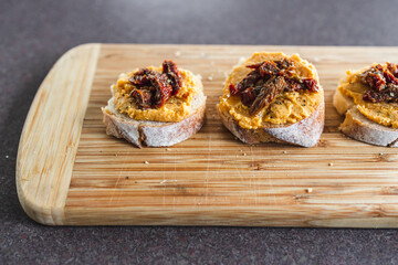 plant-based food, vegan snack with paprika hummus on sliced baguette bread topped with sundried tomatoes