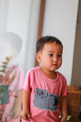 Fototapeta premium An Asian boy in a pink dress is leaning against a glass wall or reflecting window.
