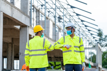 Construction Worker greeting with elbows while wearing protective face masks in building construction site during coronavirus epidemic.