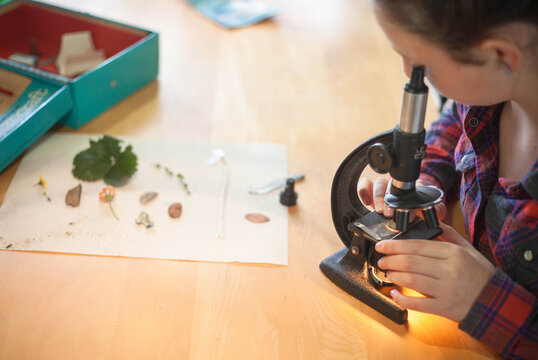Young girl looking at various things through an old school microscope in her home