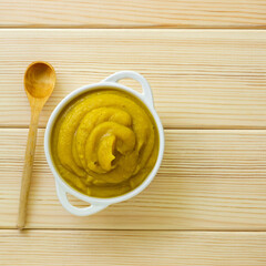 Pumpkin puree in white bowl on a light wooden background, top view