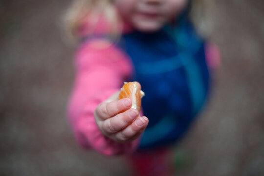 Child offers orange in her hand.