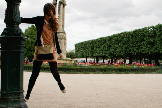 Young woman swings on light post in Paris