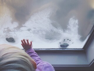 young girl making on handprints on frosty window