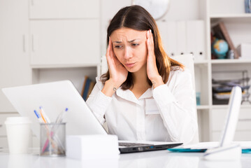 Tired young girl manager with laptop and documents working at office table