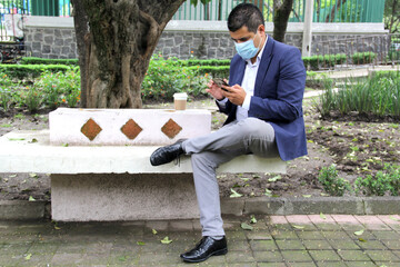 Latino adult man with protection mask and coffee, making video call with mobile phone and...