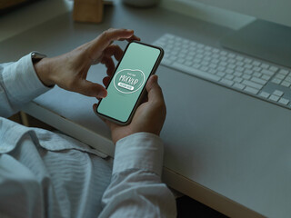 Male office worker using mock up smartphone while sitting at computer desk
