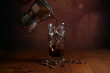 Close up view of pouring coffee into glass with ice on wooden table