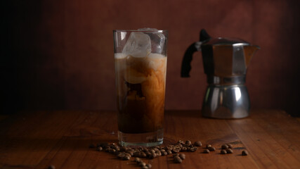 Close up view of a glass of ice latte coffee with coffee pot on wooden desk