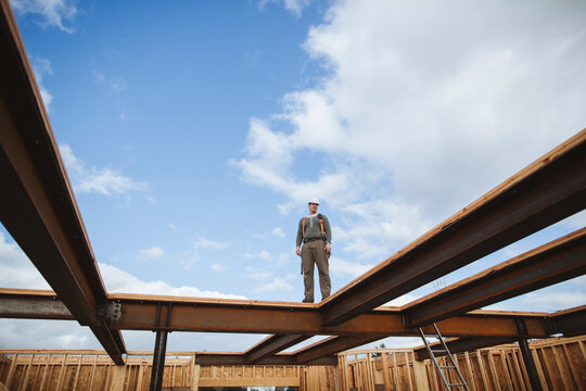 Carpenter man surveys construction site from steel beams