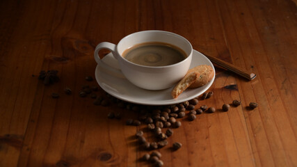 A cup of hot coffee with biscuit and coffee beans decorated on wooden table