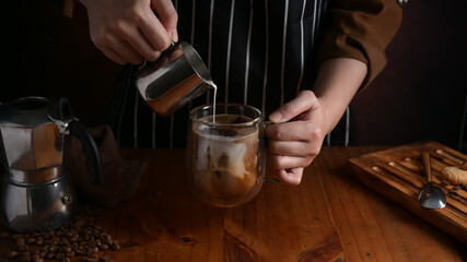 Barista pouring milk into a cup of coffee on wooden counter bar in coffee shop