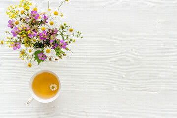 Wild flowers bouquet with cup tea on a table, top view