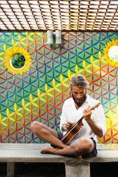 Hippie man playing ukulele in front of colorful flower of life wall