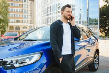 A handsome young businessman standing next to his car and talking on his phone