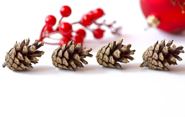 Pine cones, blurred red holly berries and Christmas ball on white