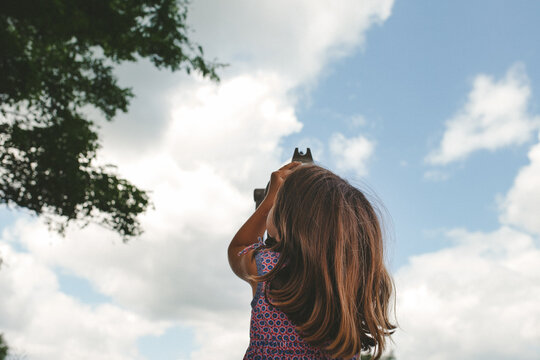 Little girl looks up at clouds through view finder