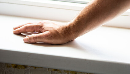 
Male hands on a white plastic window sill. Against the background of the window. Hand gestures. Close-up. Place for an inscription.