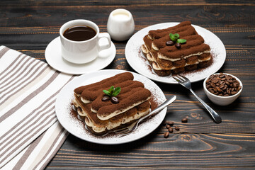 Two portions of Classic tiramisu dessert, cup of coffee and milk or cream on wooden background