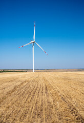 One windmill stands in a mown field against a blue sky.