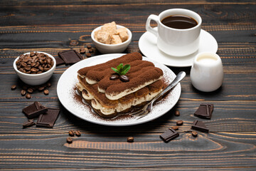 portion of Classic tiramisu dessert, cup of coffee and milk or cream on wooden background