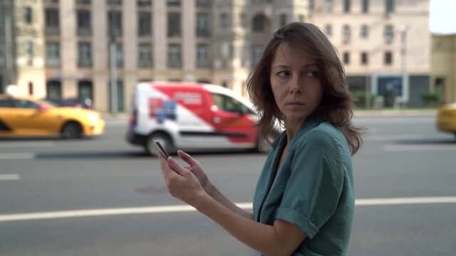 middle aged woman in a state of depression walks along the road in the city and looks at the mobile phone screen