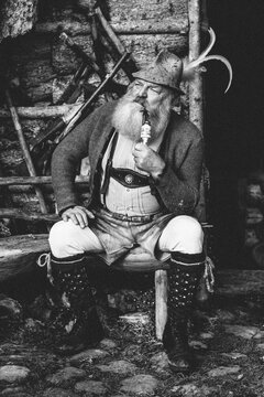 old bearded man in typical austrian lederhosen sitting on a bench smoking a pipe