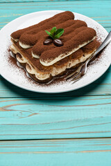 portion of Classic tiramisu dessert on ceramic plate on colorful blue wooden background