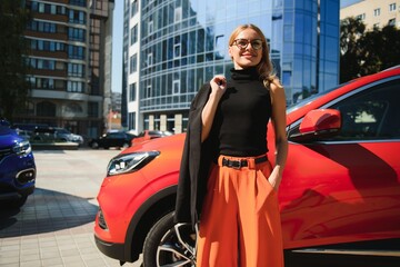 Naklejka premium Yong pretty woman standing near a big all terrain car outdoors. Driver girl in casual clothes outside her vehicle.