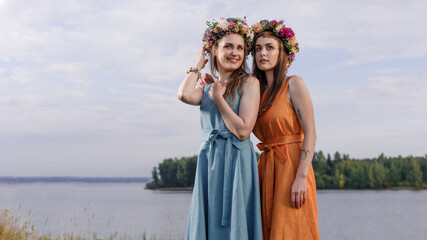 Two young and lovely girls in flower wreaths in nature. Ancient pagan origin celebration concept. Summer solstice day. Mid summer. Ancient rituals.