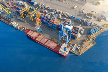 Aerial top view huge cargo ship moored at the pier at the port, loading goods, ore mineral bulk...