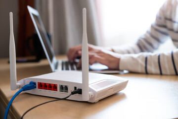 Selective focus at router. Internet router on working table with blurred man connect the cable at the background. Fast and high speed internet connection from fiber line with LAN cable connection. - obrazy, fototapety, plakaty