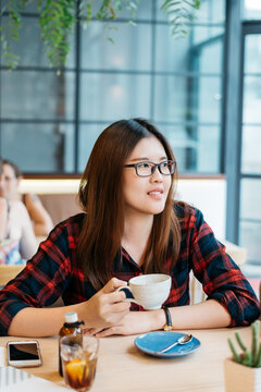 Smiling asian woman drinking coffee at the cafe