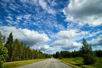 Beautiful landscape with blue sky, white clouds and the road that goes to the horizon with the forest and trees on the roadsides