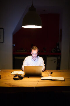 Young man working overtime in a dark office behind his laptop