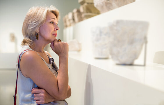 Mature positive spanish woman standing in art museum near the antique sculpture
