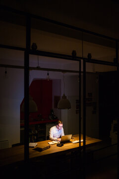 Young man working overtime in a dark office behind his laptop