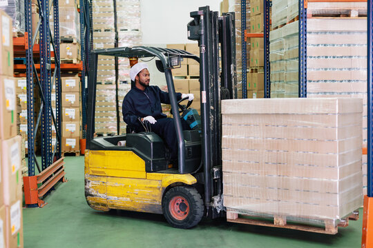 Young male worker driving a forklift in a warehouse.