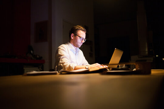 Young man working overtime in a dark office behind his laptop