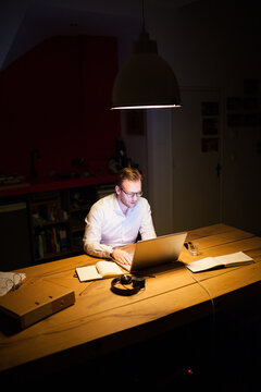 Young man working overtime in a dark office behind his laptop
